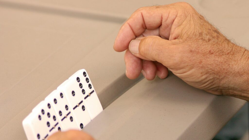 the hands of an older gentleman playing dominoes